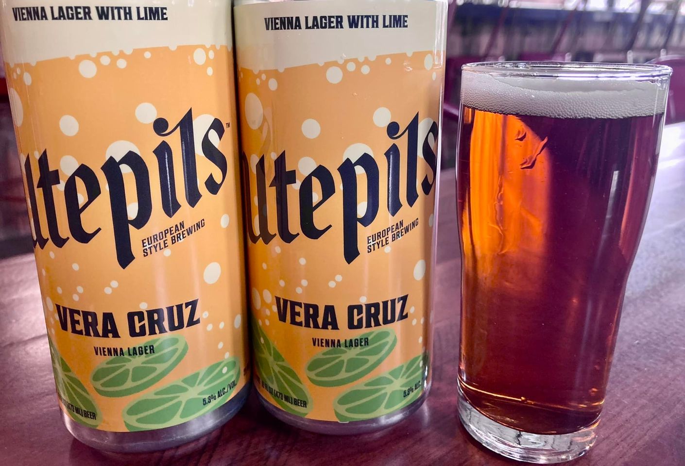 Two cans of Utepils Vera Cruz on a bar top near a full glass of beer