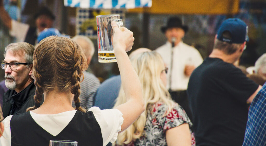 A woman in an Oktoberfest crowd raising her mug