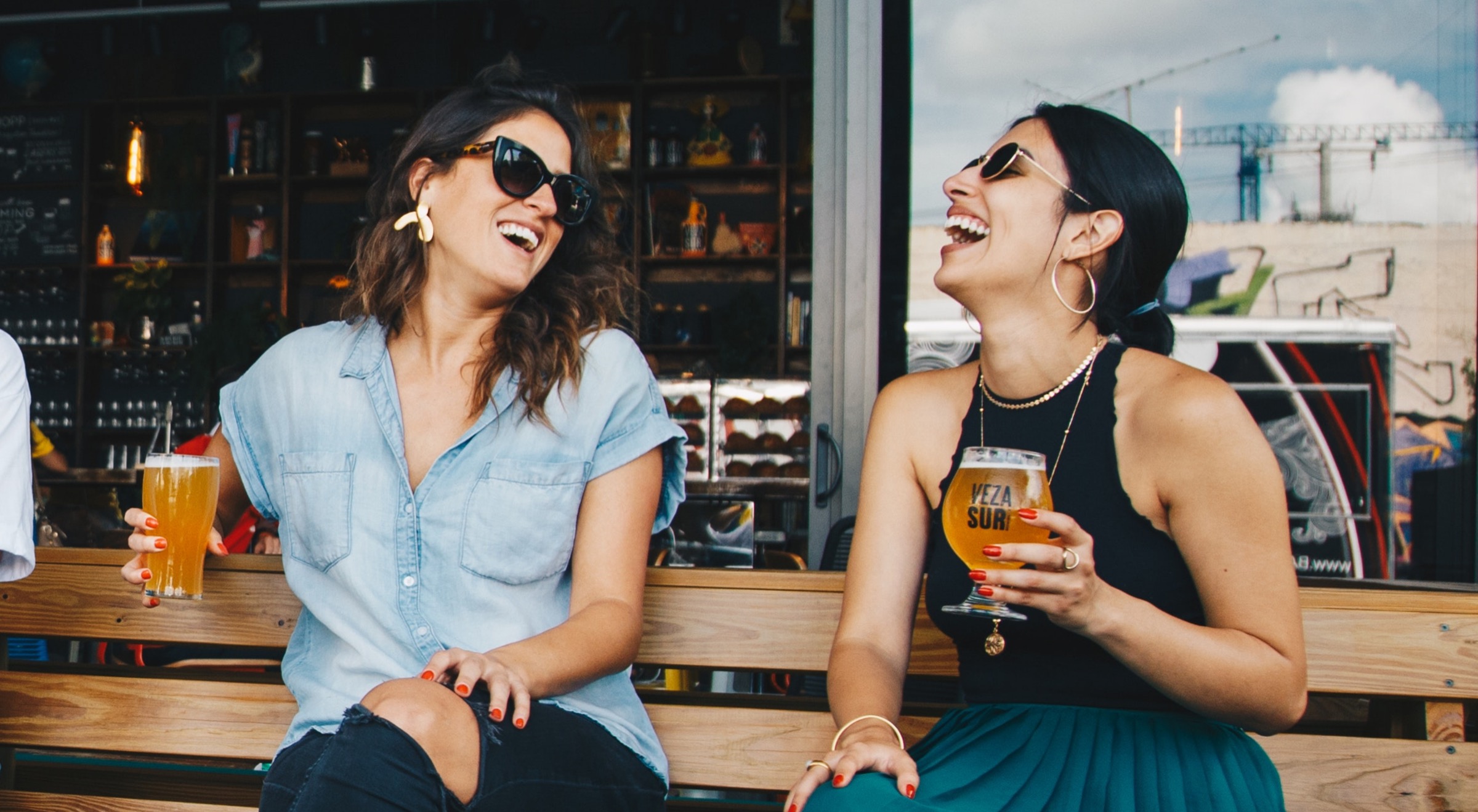 Two women drinking beer on a bench together