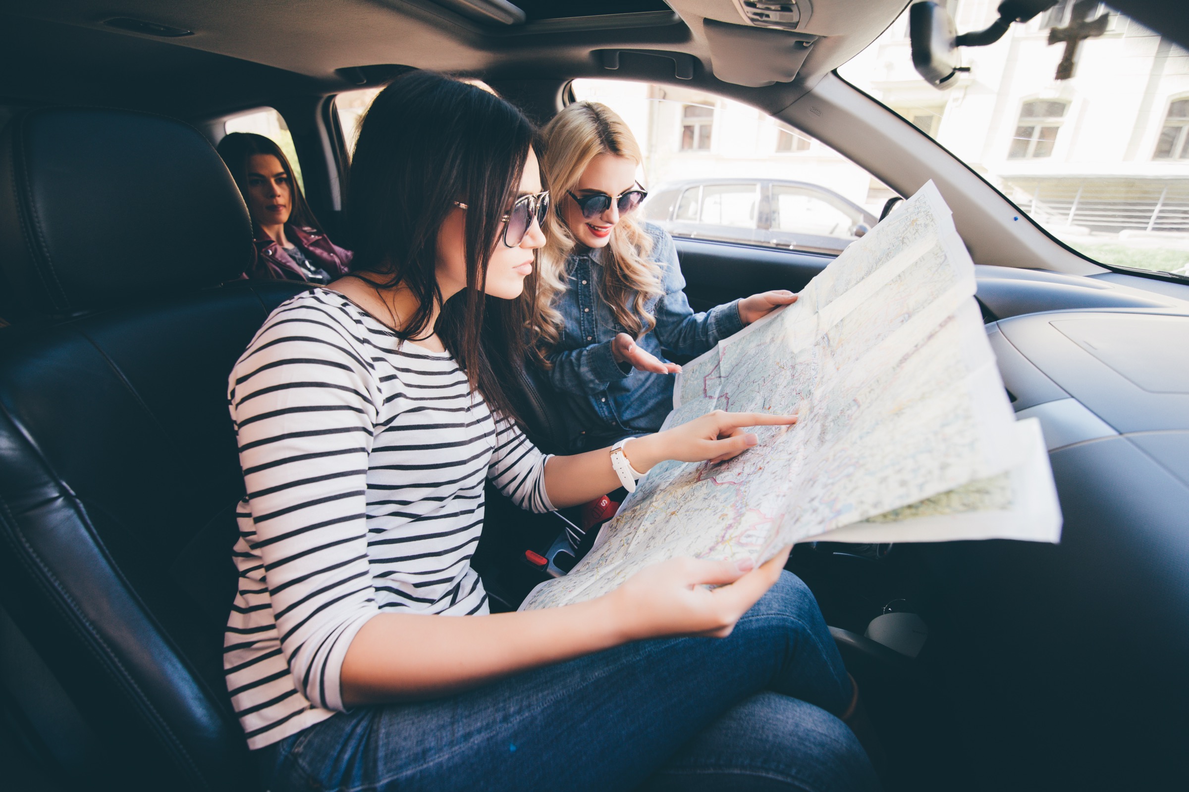 A woman drives a car while the woman next to her navigates on a map